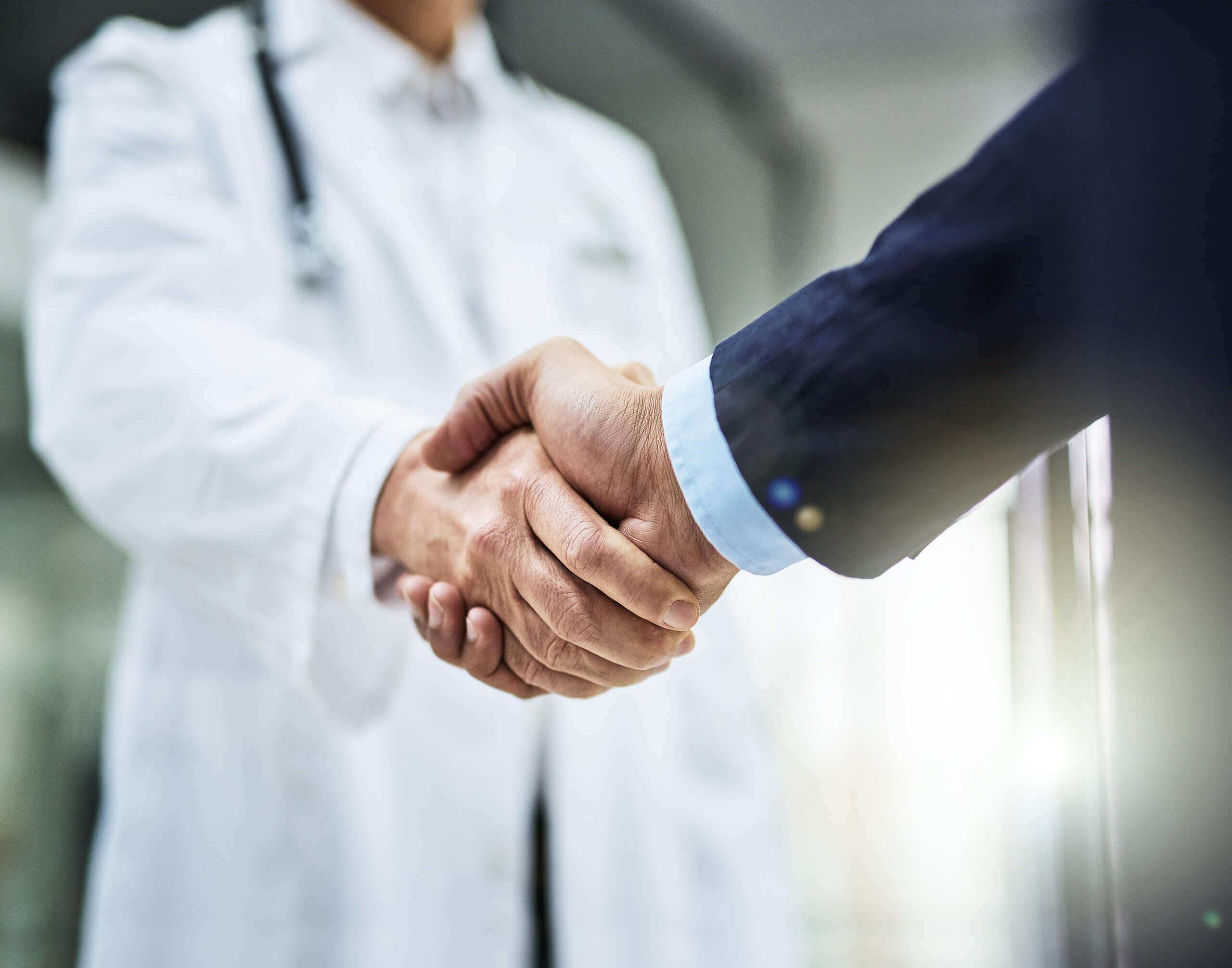 Showing a person in a lab coat shaking hands with a person wearing a business suit.